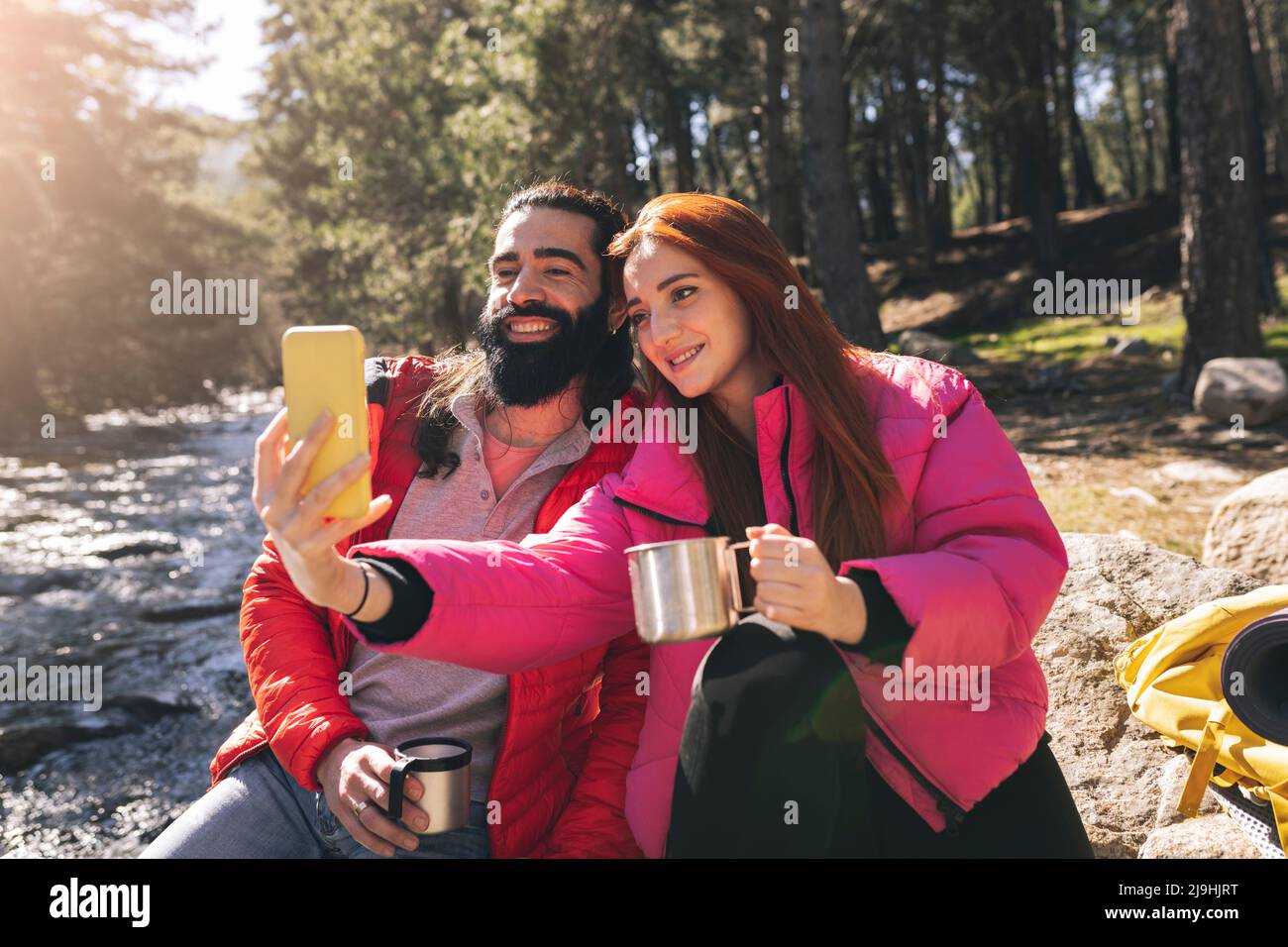Giovane donna che prende selfie con uomo bearded attraverso il telefono intelligente in giorno di sole Foto Stock