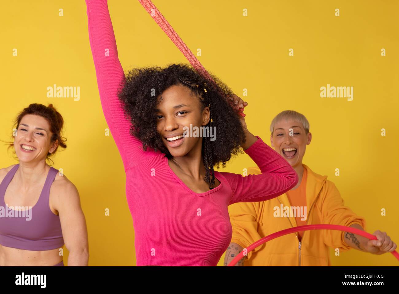 Donna sorridente che si esercita con banda di resistenza su sfondo giallo Foto Stock