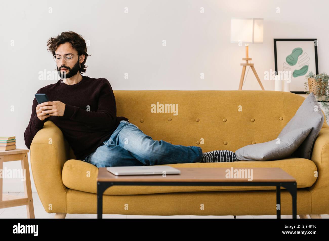 Uomo che utilizza il telefono cellulare sul divano nel soggiorno di casa Foto Stock