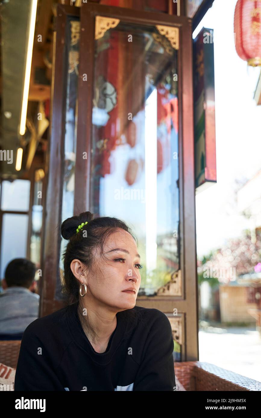 donna asiatica seduta tristemente in una caffetteria con occhi teari Foto Stock