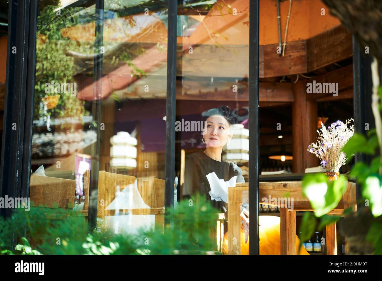 donna asiatica seduta in una caffetteria o in una casa da tè guardando attraverso il vetro della finestra Foto Stock