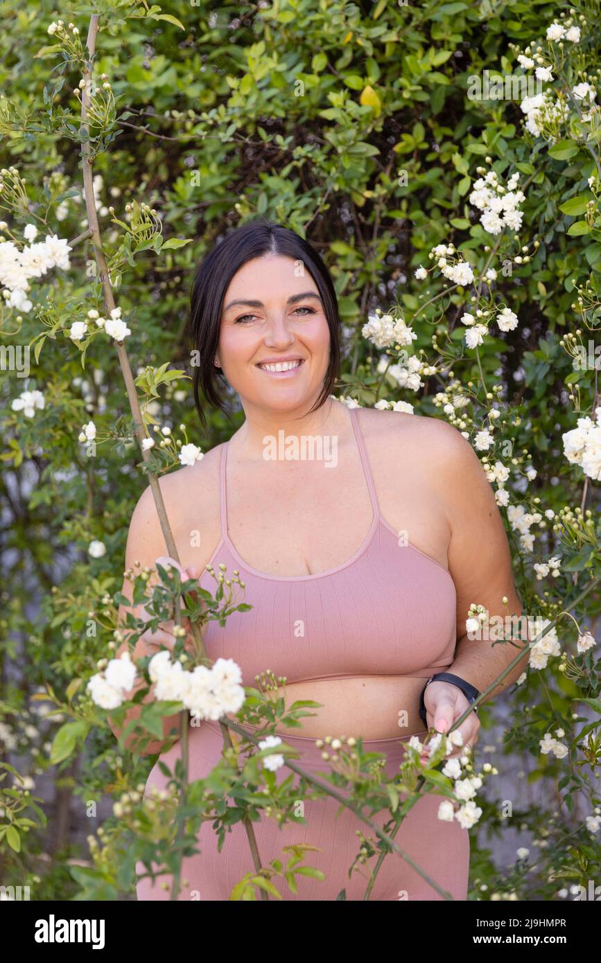 Sorridente donna più taglia in piedi in mezzo ai fiori Foto Stock