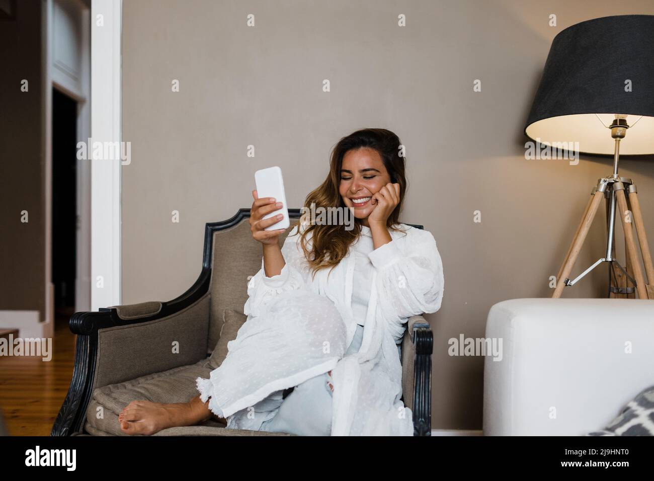 Donna felice con smartphone seduto in poltrona a casa Foto Stock