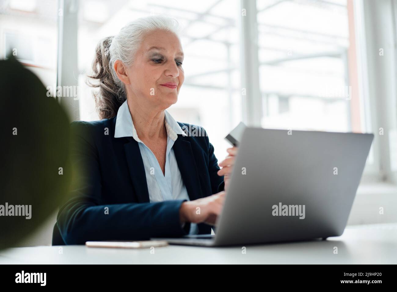 Donna d'affari sorridente con scheda di lavoro sul portatile in ufficio Foto Stock