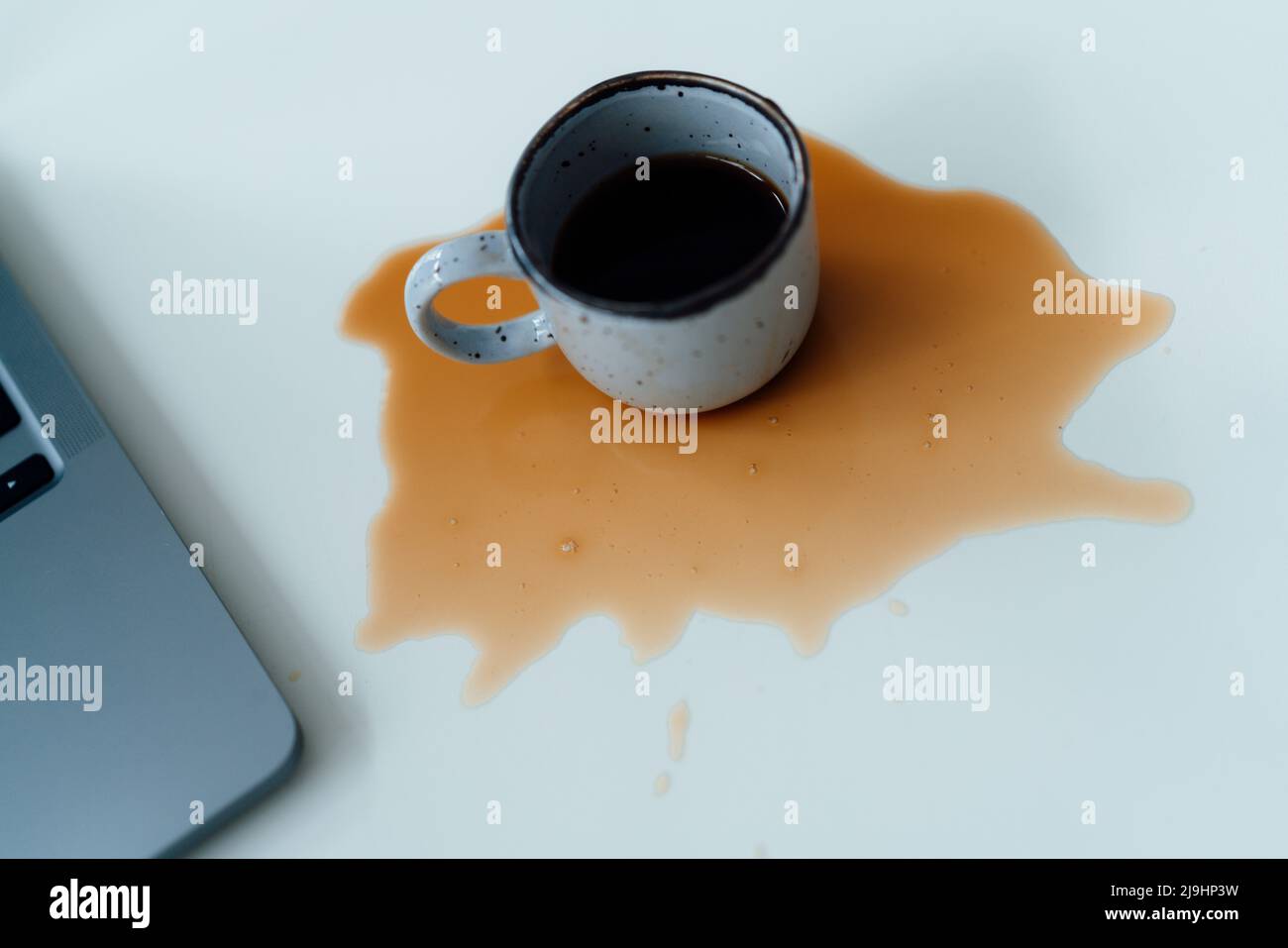 Caffè versato da un computer portatile sulla scrivania Foto Stock