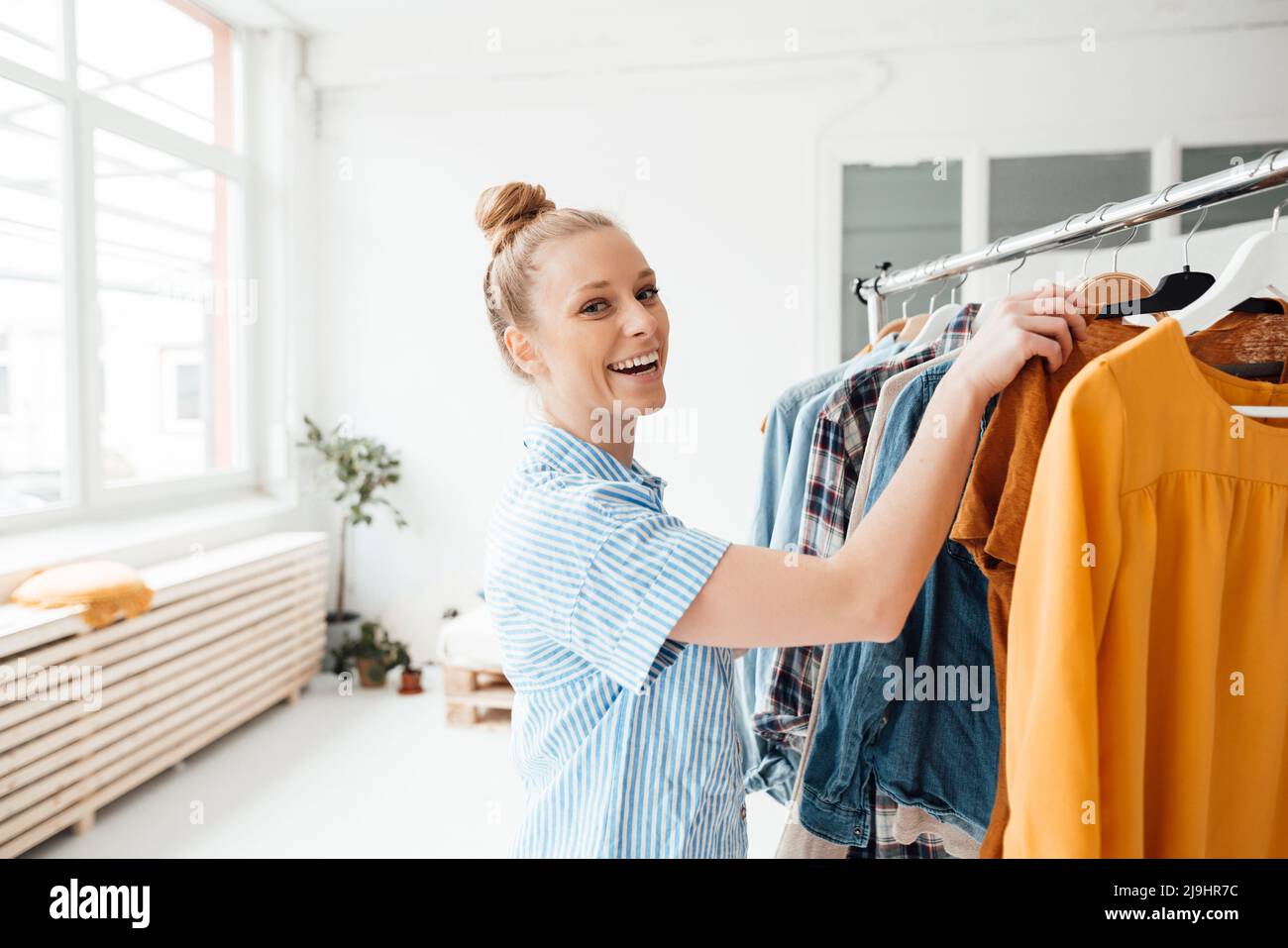 Happy moda designer appendere abiti su scaffale in studio Foto Stock