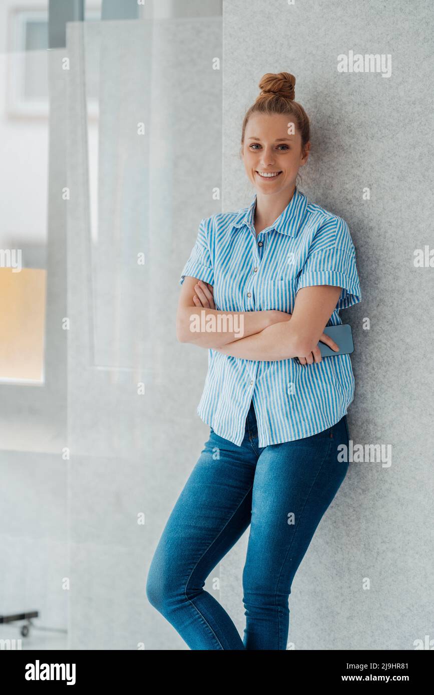 Stilista sorridente con braccia incrociate appoggiate a parete in studio Foto Stock