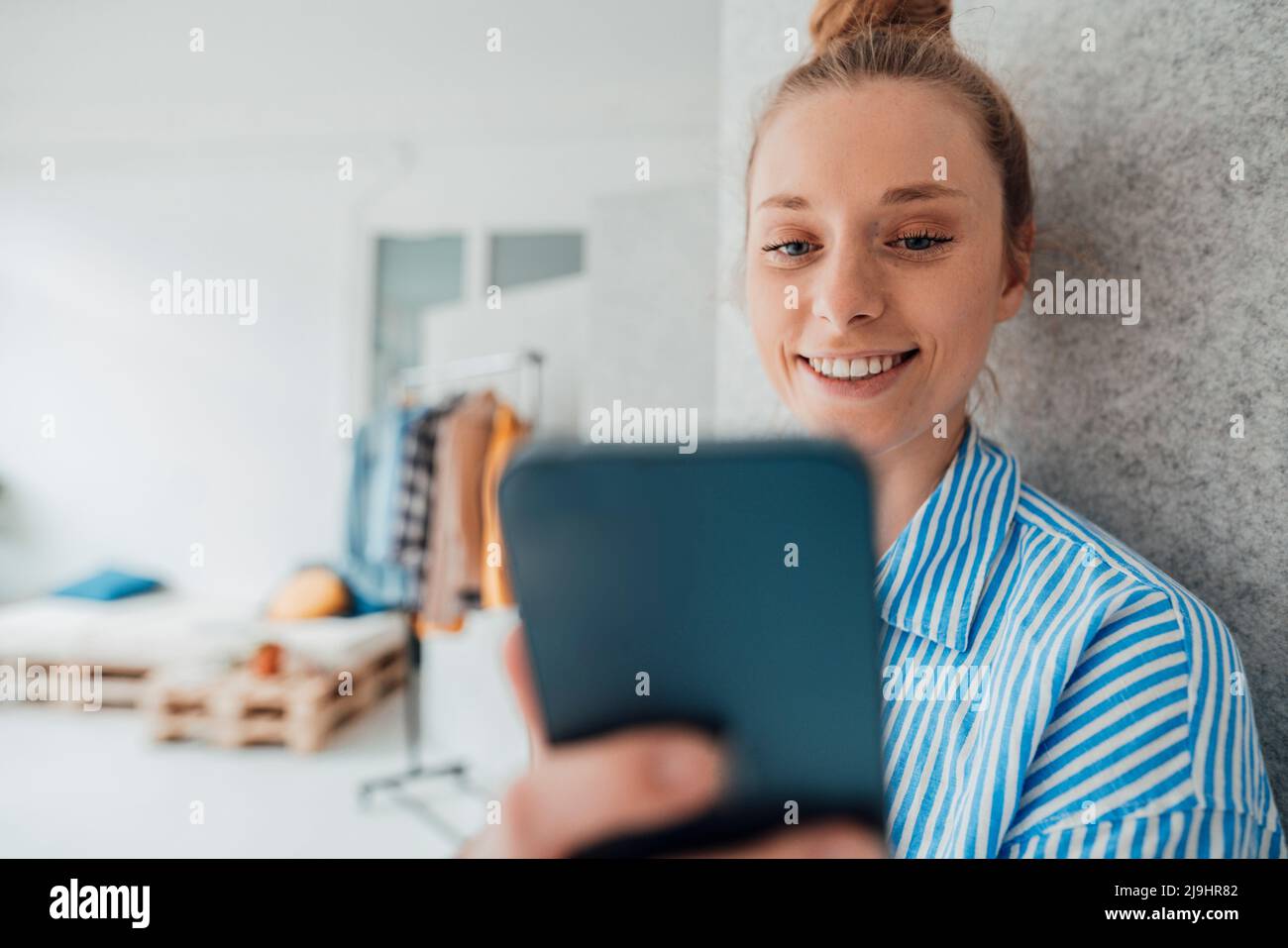 Buon stilista di moda utilizzando smartphone vicino alla parete in studio Foto Stock