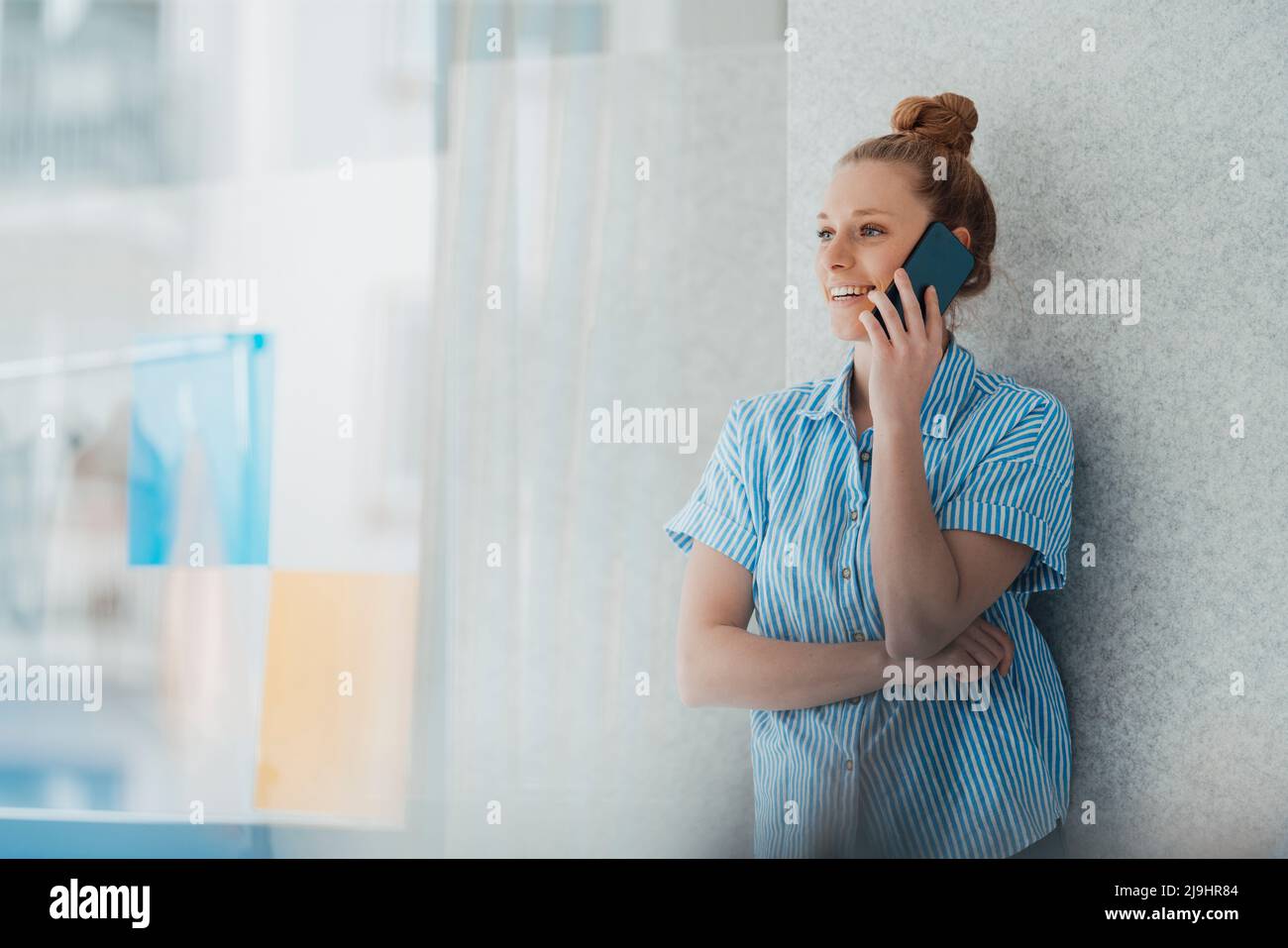 Giovane stilista di moda che parla su smartphone vicino alla parete in studio Foto Stock
