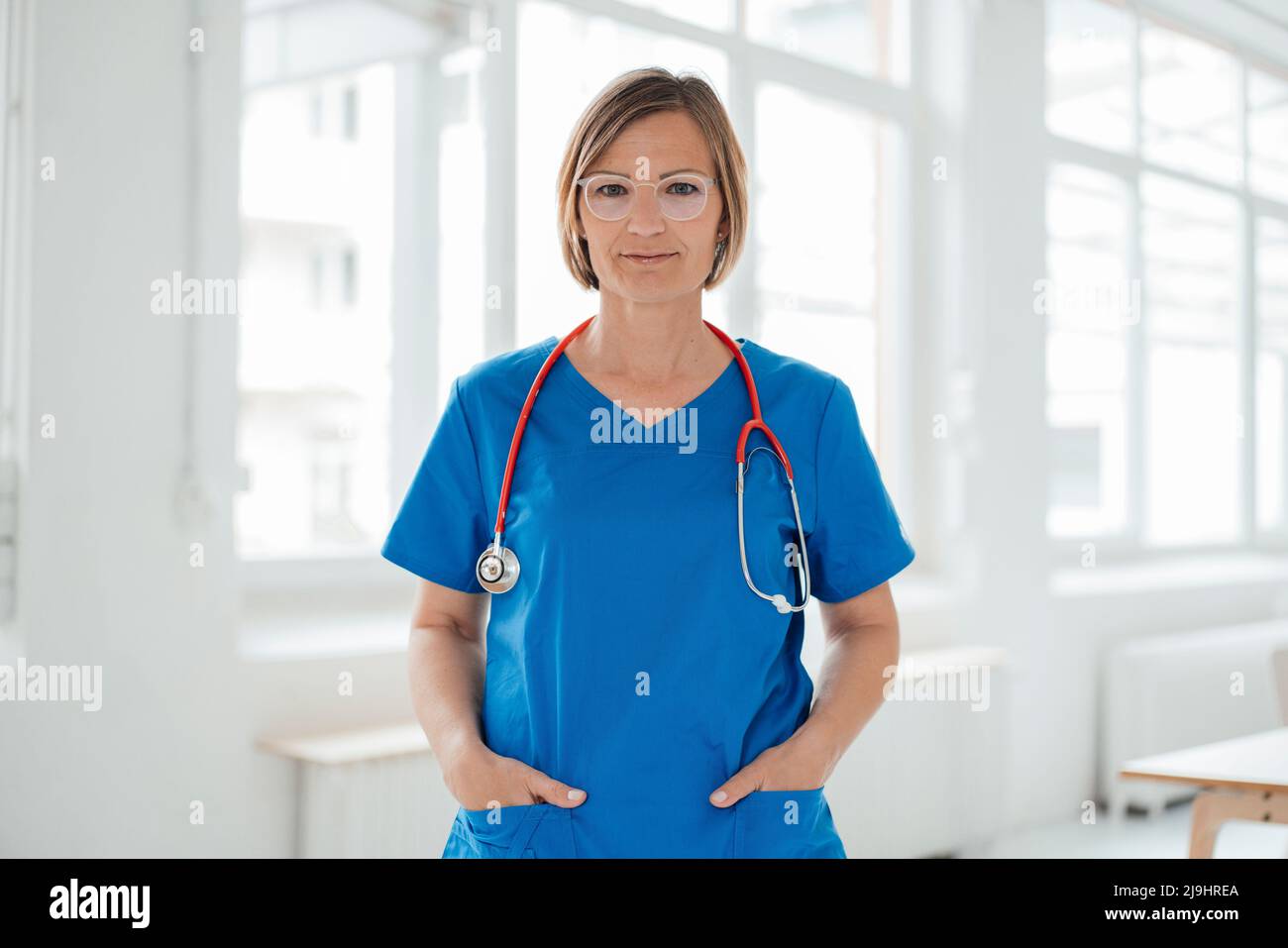 Medico sorridente in piedi con le mani in blu scrub tasche in ospedale Foto Stock