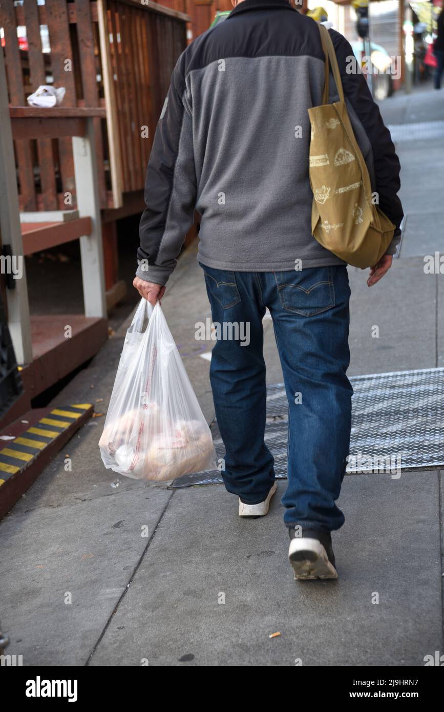 Un uomo porta con sé un sacchetto di plastica di generi alimentari mentre cammina lungo un marciapiede nel quartiere Chinatown di San Francisco, California. Foto Stock