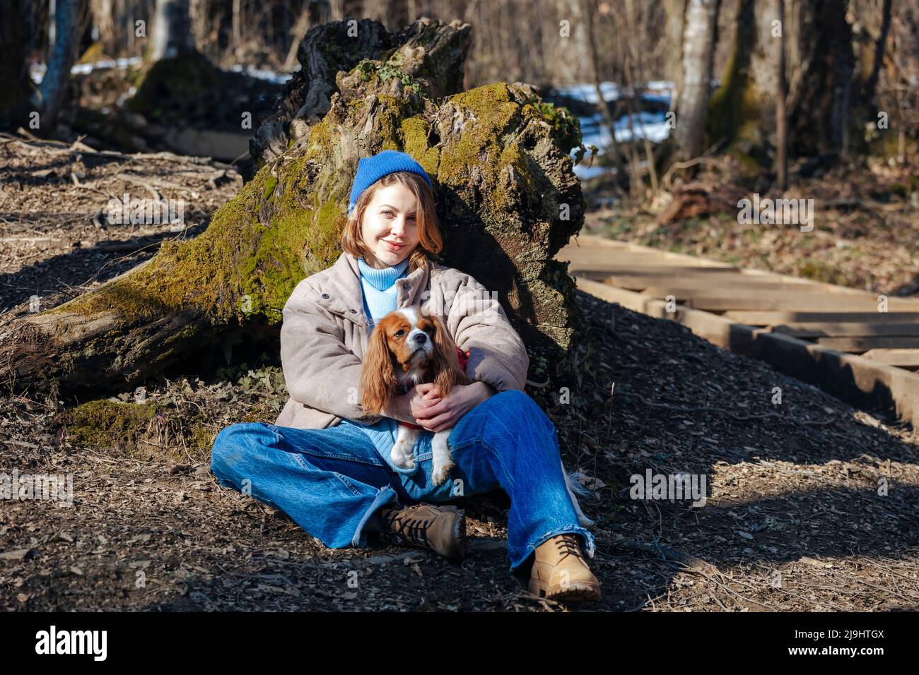 Giovane donna sorridente con cane da compagnia seduto nella foresta il giorno di sole Foto Stock