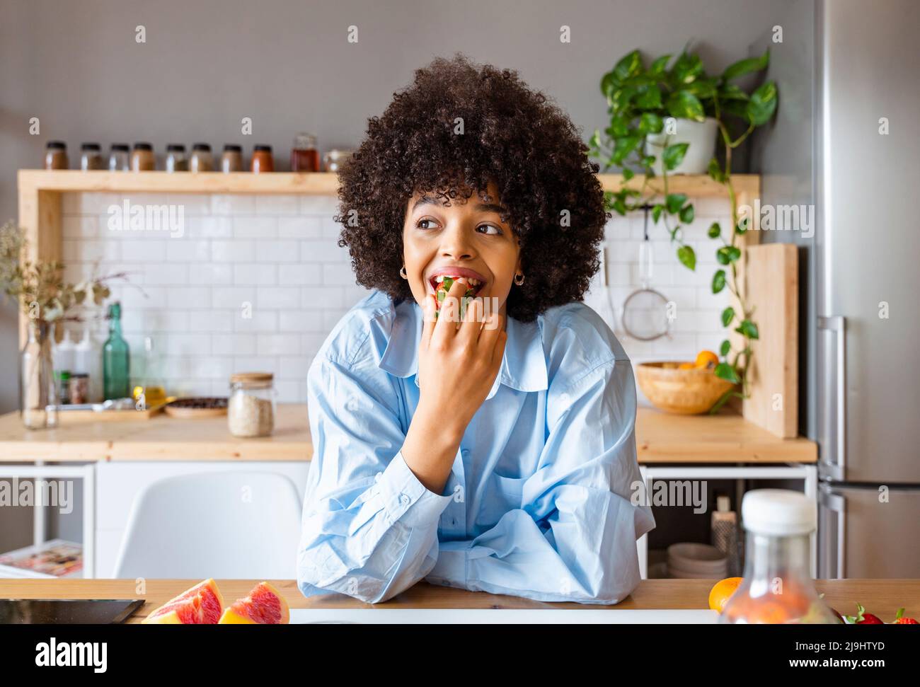Bella donna che mangia fragola appoggiata a casa sull'isola della cucina Foto Stock