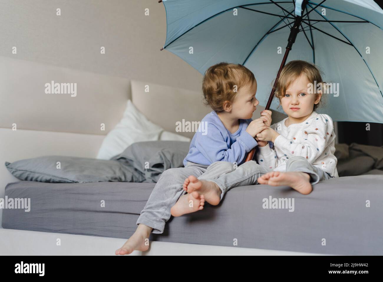 Le sorelle gemelle sono sedute con ombrello sul letto di casa Foto Stock