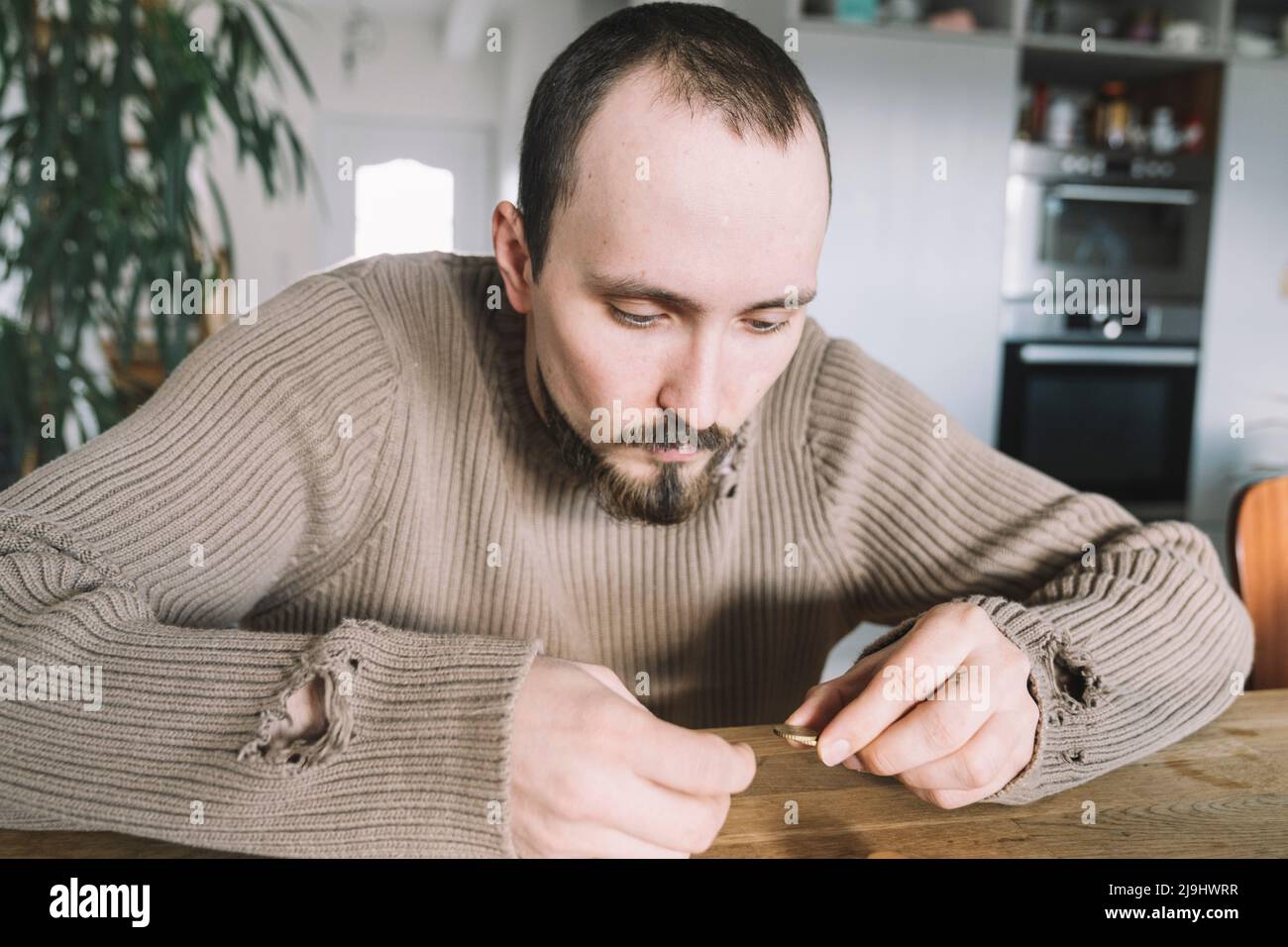 Giovane uomo con pullover strappato seduto a casa contando denaro Foto Stock