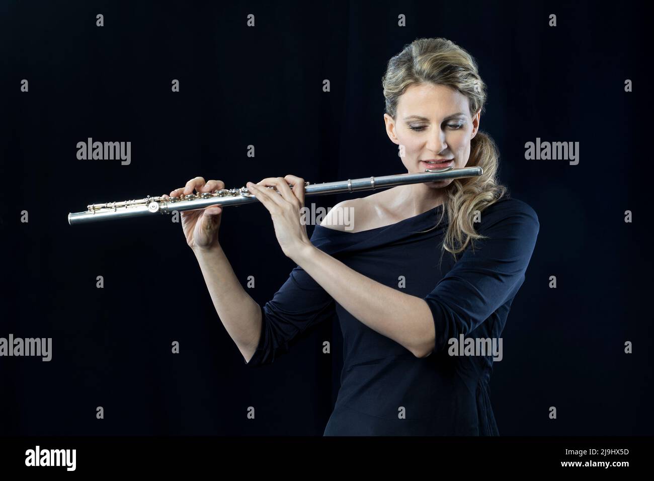 Donna matura che gioca flauto su sfondo nero Foto Stock