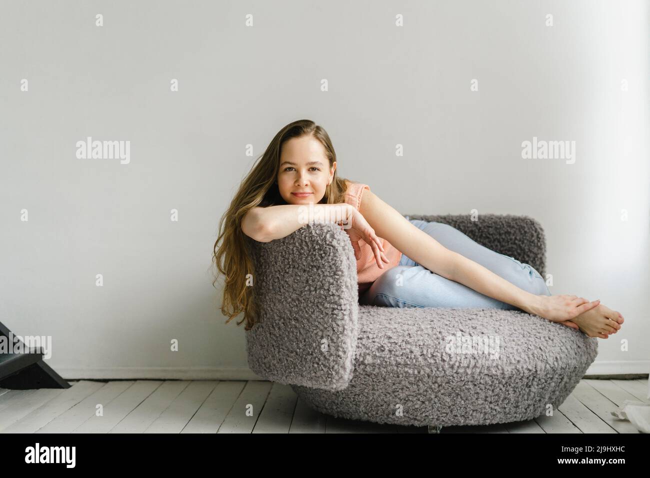 Donna sorridente seduta su poltrona a casa Foto Stock