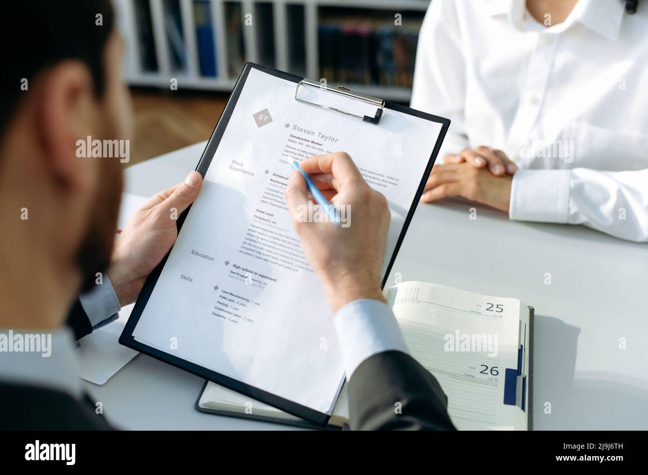 Primo piano di un ripristino del processo. Lo specialista delle assunzioni, si siede a una scrivania in ufficio, conduce un colloquio con il candidato quando si fa domanda per un lavoro, ha messo a fuoco legge il curriculum del candidato, prende una decisione Foto Stock