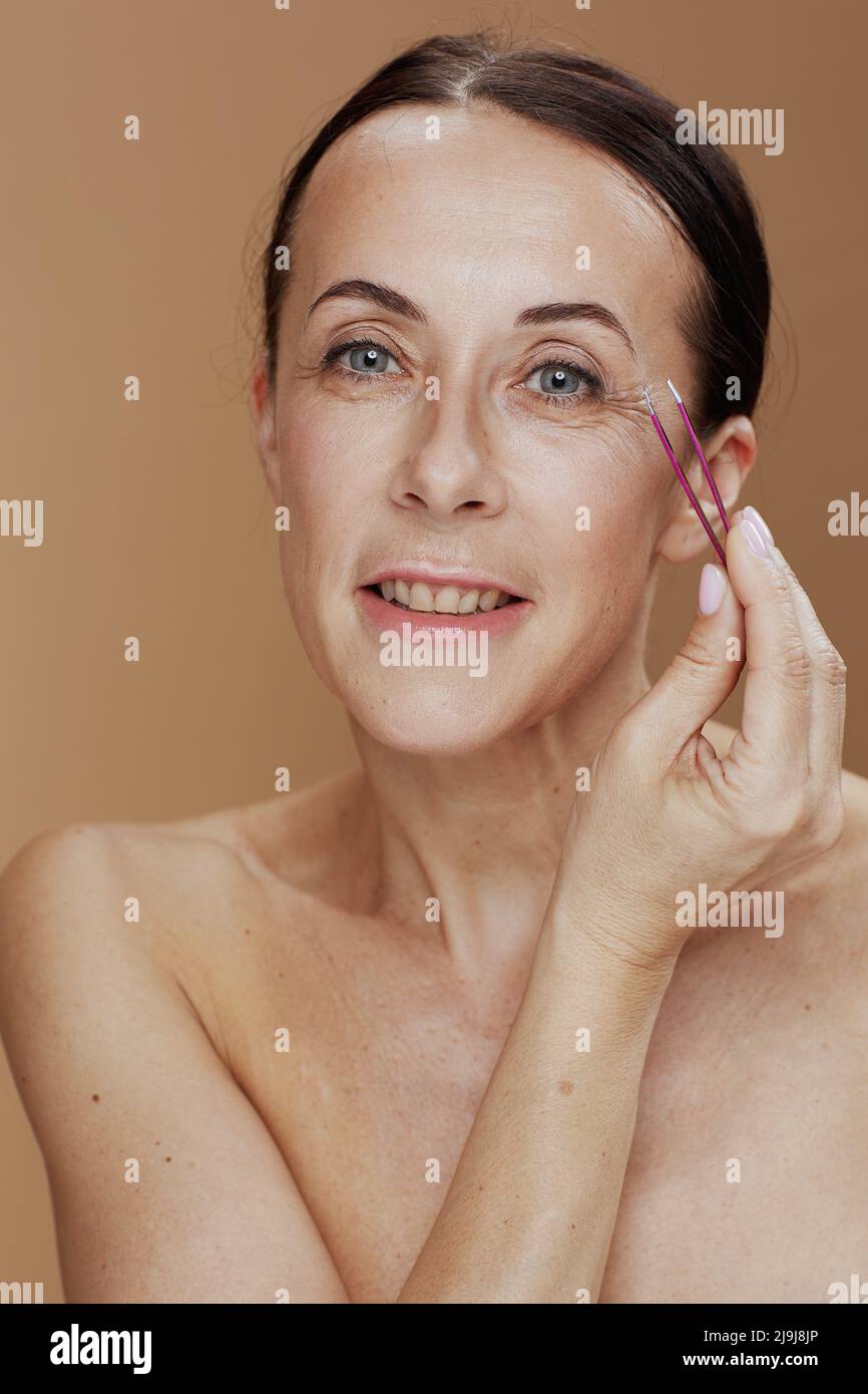 Ritratto di donna moderna con pinzette su sfondo beige. Foto Stock