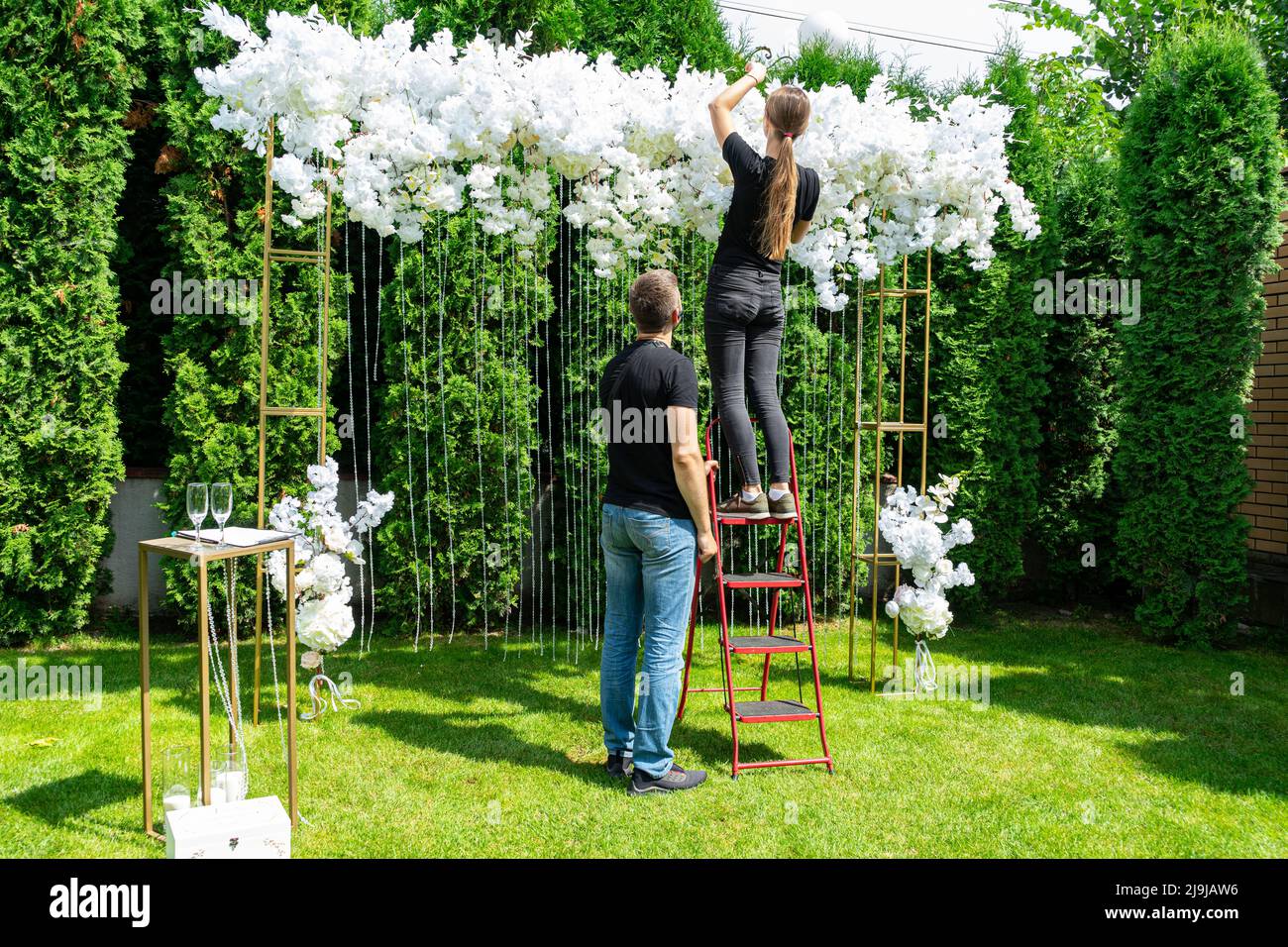 Donna e uomo decorare l'area foto matrimonio con fiori bianchi su un prato verde. Foto Stock