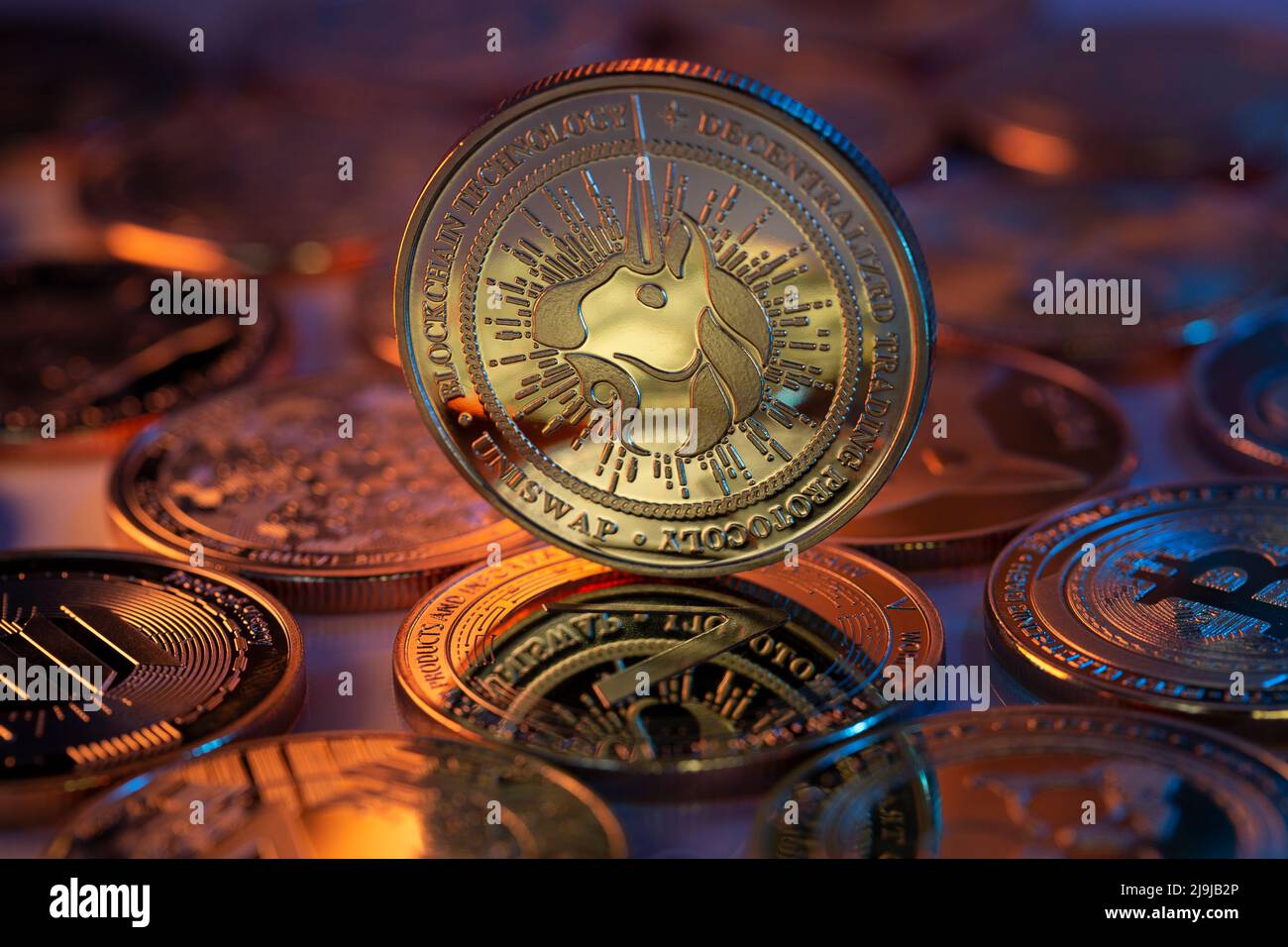 Uniswap UNI Cryptocurrency Coin fisico posto su cripto altcoins e illuminato con luci arancioni e blu. Scatto macro. Messa a fuoco selettiva. Foto Stock