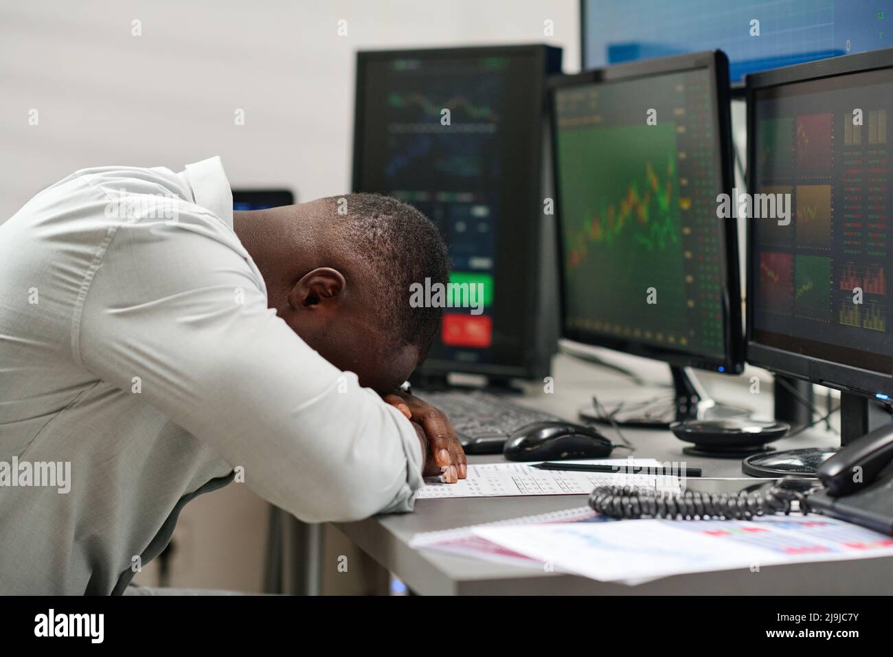 Esausto giovane afroamericano che lavora in agenzia di brokeraggio avendo burnout posare la testa sulla scrivania Foto Stock