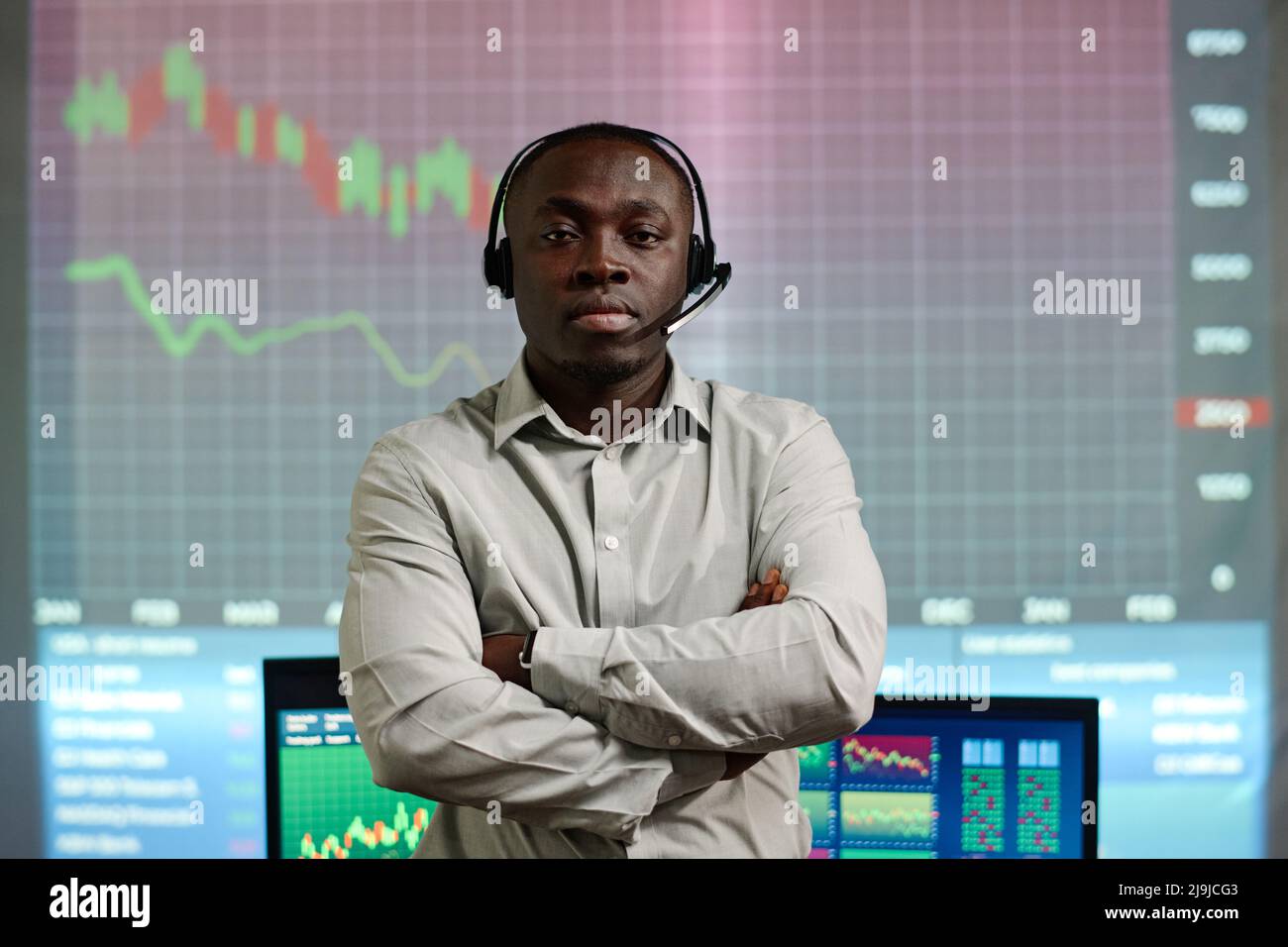 Ritratto di un esperto di investimenti che indossa cuffie con microfono in piedi in ufficio con braccia incrociate guardando la fotocamera Foto Stock