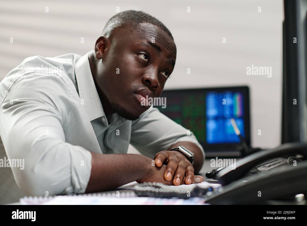 Giovane broker afroamericano estremamente stanco al lavoro guardando le carte di borsa su schermi di computer Foto Stock