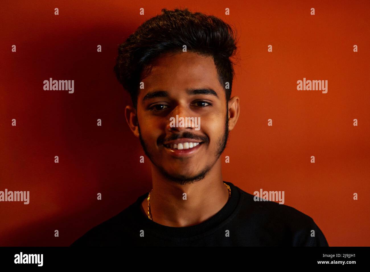 Verifica biometrica. Rilevamento del viso umano, alta tecnologia. Uomo indiano studente che tiene telefono ID volto scansione sfondo arancione parete Foto Stock