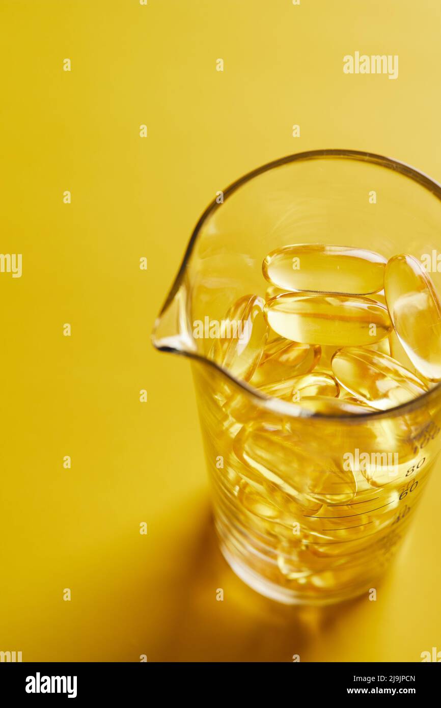Capsule di acido grasso Omega-3 su sfondo blu in un bicchiere. Il concetto di medicina e di vita sana. Foto verticale. Foto Stock