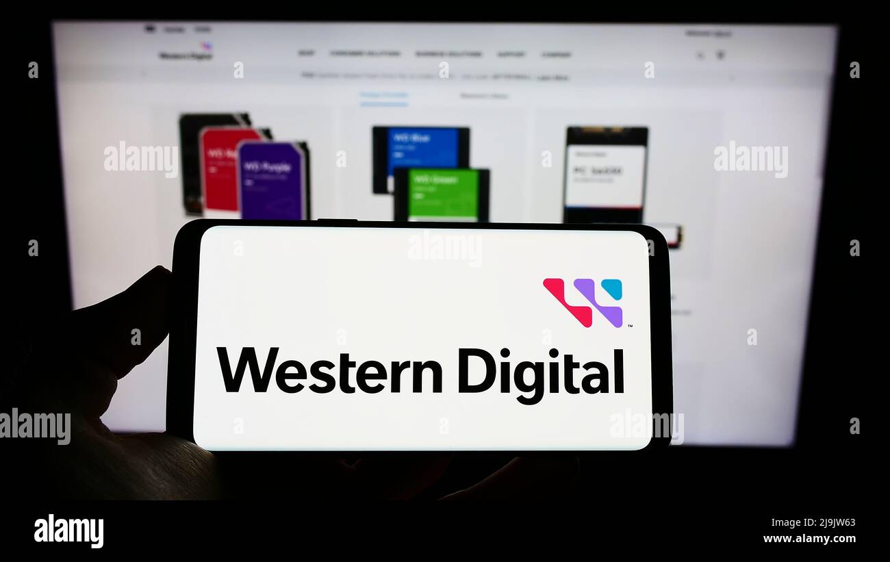 Persona che tiene il cellulare con il logo della società americana Western Digital Corporation (WDC) sullo schermo di fronte alla pagina web. Mettere a fuoco sul display del telefono. Foto Stock