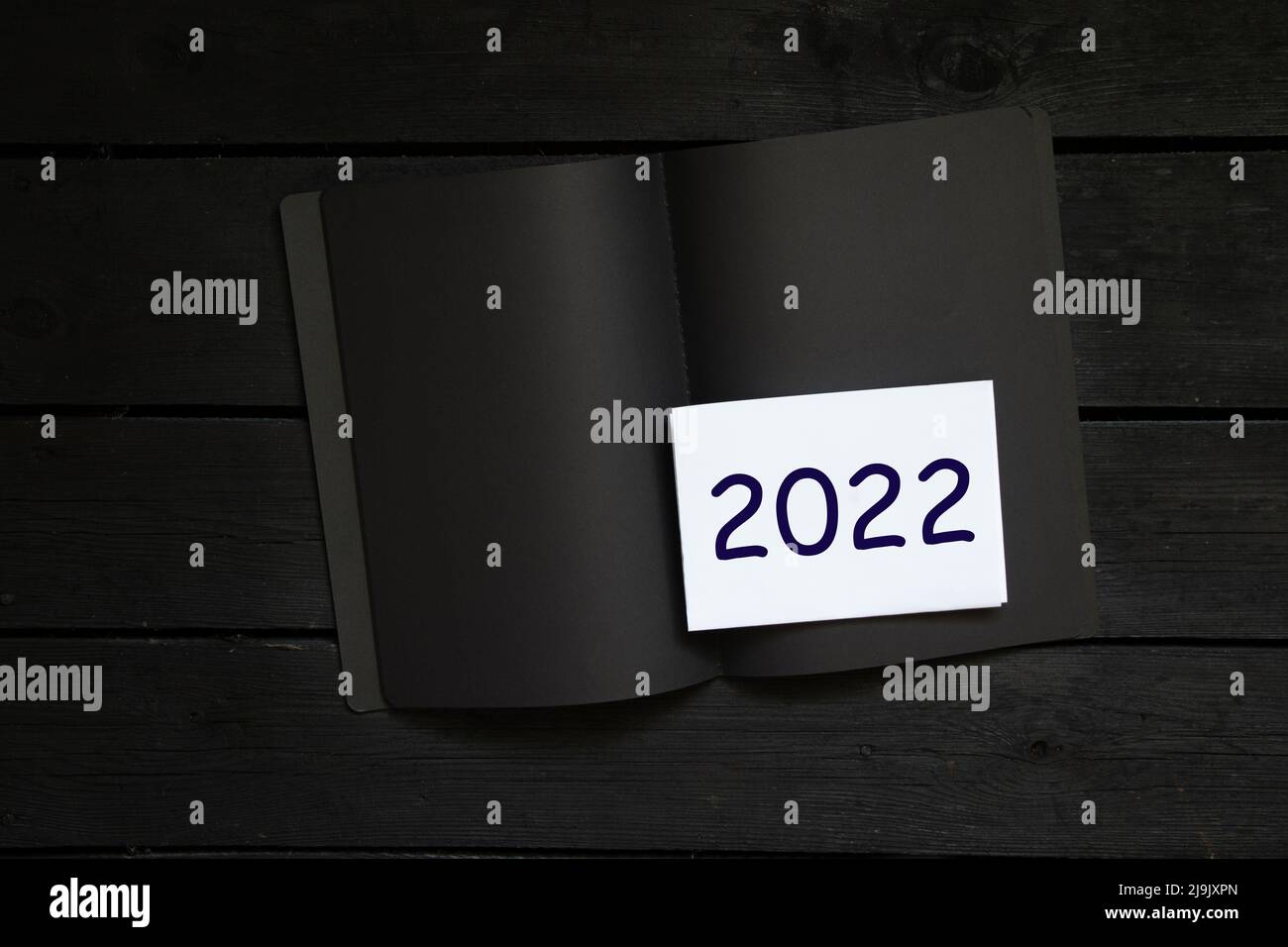 taccuino nero con foglio bianco e testo su di esso 2022 su tavola in legno nero, iscrizione 2022 su foglio bianco, felice anno nuovo 2022 Foto Stock
