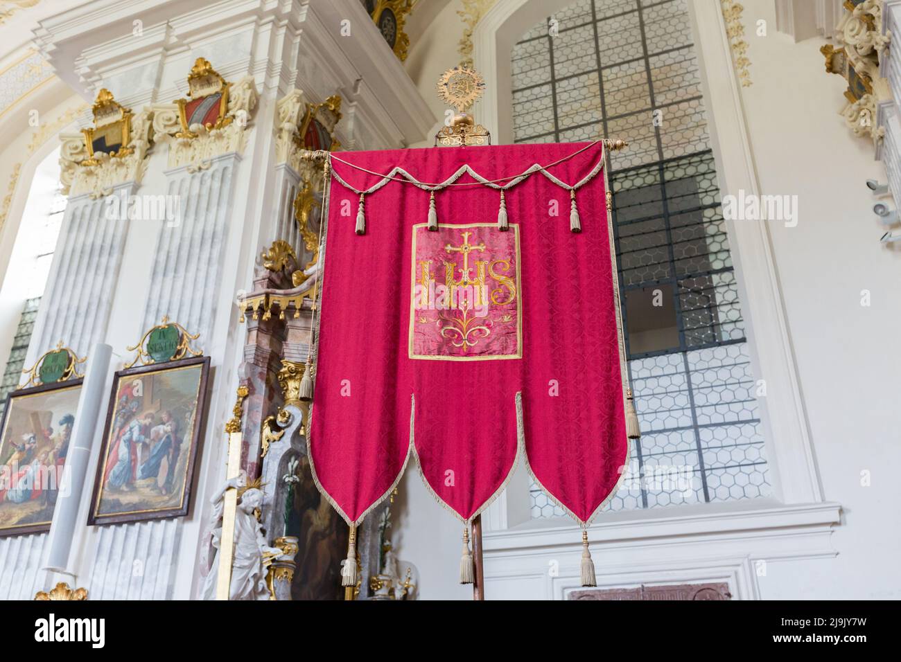 Raitenhaslach, Germania - 25 luglio 2021: Standard rosso con il monogramma di Gesù 'IHS'. All'interno della chiesa di Raitenhaslach Abbey. Foto Stock