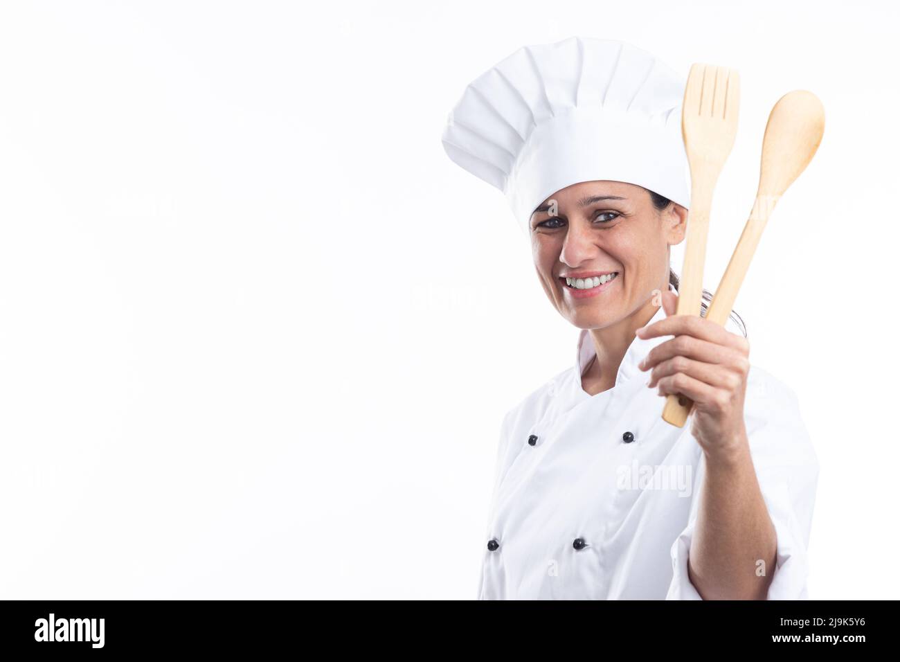Ritratto di felice donna caucasica guardando la macchina fotografica in abito chef con utensili da cucina in mani isolate su sfondo bianco con spazio copia. Foto Stock