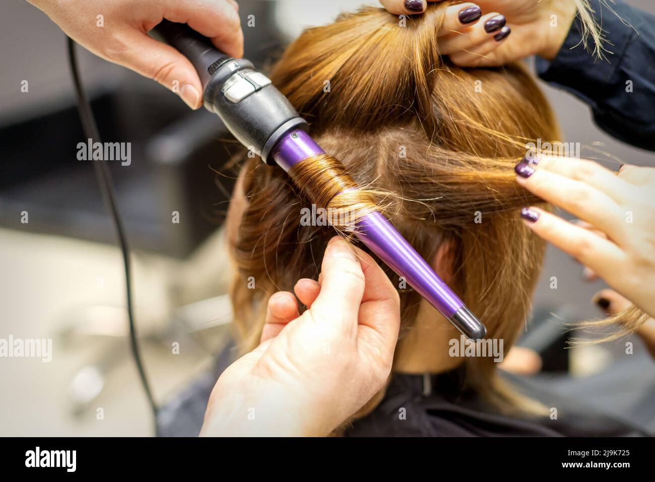 L'acconciatore ricci acconciature di capelli lunghi marrone con il ferro  arricciacapelli in parrucchiere, primo piano Foto stock - Alamy