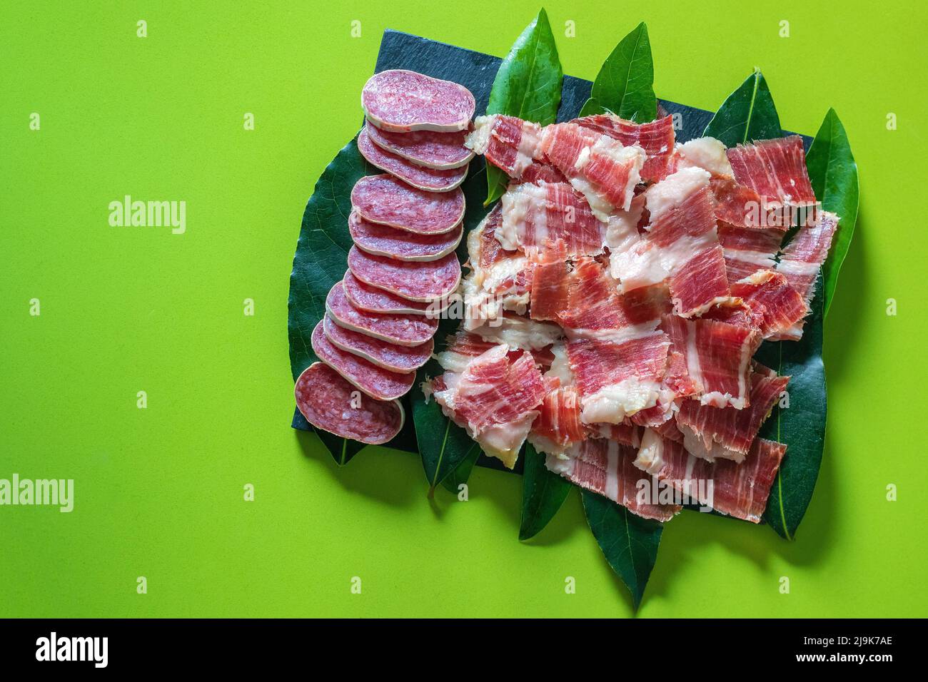 Fuet, salsiccia affettata e prosciutto iberico spagnolo su sfondo verde. Salsiccia spagnola. Gastronomia e cibo in Spain.Traditional Spanish Jamon Serrano prosciutto. Foto Stock