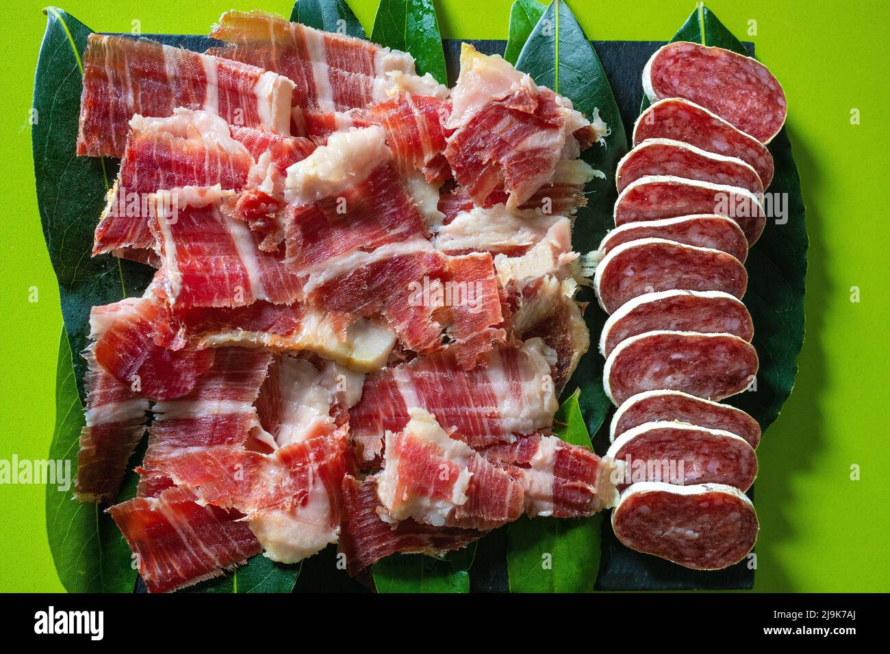 Fuet, salsiccia affettata e prosciutto iberico spagnolo su sfondo verde. Salsiccia spagnola. Gastronomia e cibo in Spain.Traditional Spanish Jamon Serrano prosciutto. Foto Stock