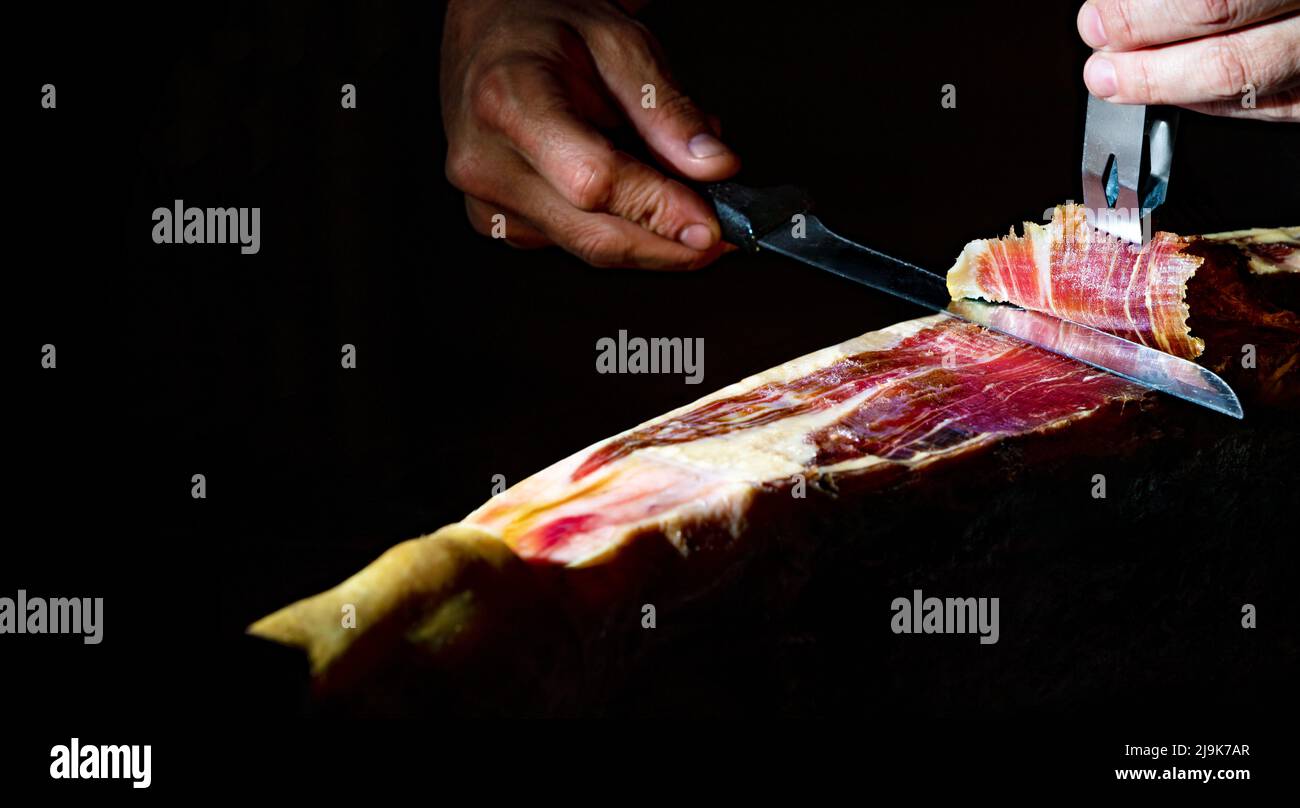 Dettaglio primo piano del maestro tagliere di prosciutto iberico su sfondo scuro. Gastronomia e cibo in Spagna. Foto Stock