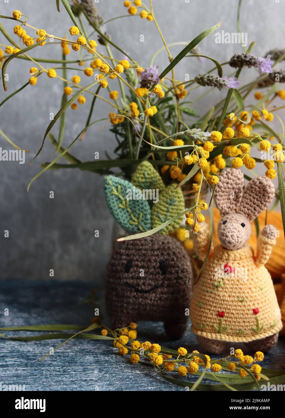 Primo piano dei giocattoli fatti a mano. Uncinetto pianta e coniglietto su sfondo grigio. Vita morta con fiori primaverili e giocattoli carini. Idee regalo di Pasqua. Foto Stock