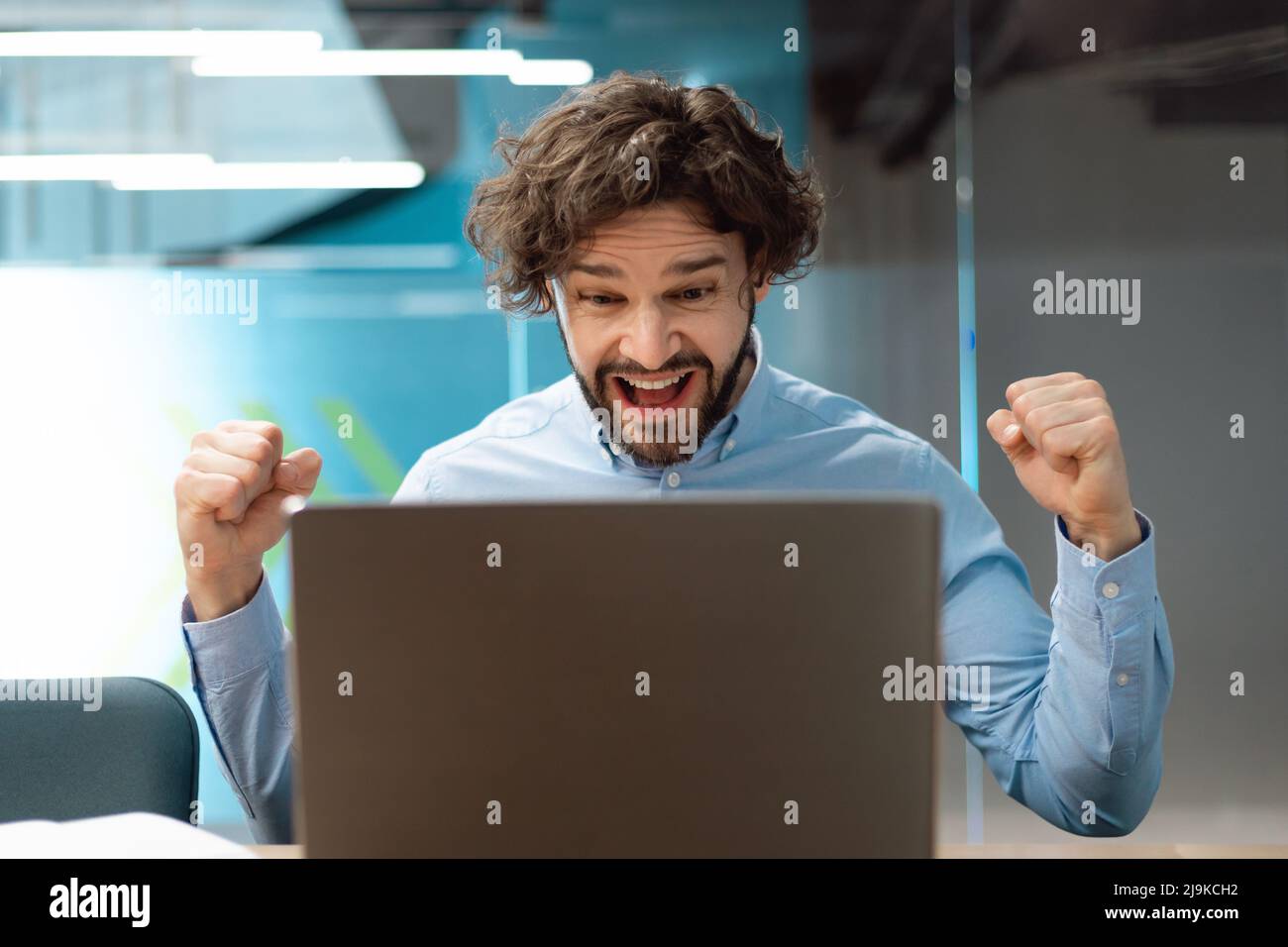 Un uomo d'affari entusiasta che utilizza il pc festeggia il successo scuotendo i pugni urlando sì Foto Stock