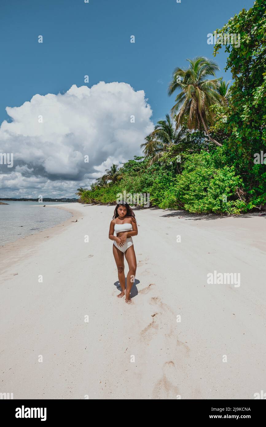 Giovane ragazza asiatica in bikini bianco su una spiaggia di sabbia bianca dell'isola tropicale circondata da palme da cocco in una giornata tropicale di sole Foto Stock
