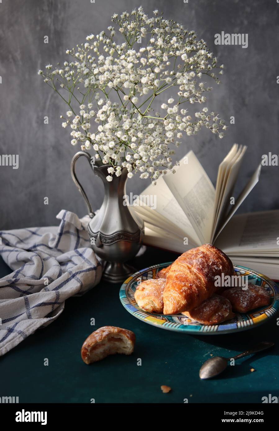 Buongiorno! Caffè nero e croissant su un tavolo. Foto soleggiata con dolci e fiori. Cibo ancora vita foto. Foto Stock