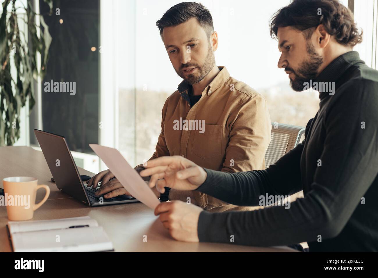 Lavoratori aziendali seri che cercano documenti, collaborano, utilizzano il laptop in un ufficio moderno, spazio per le copie Foto Stock