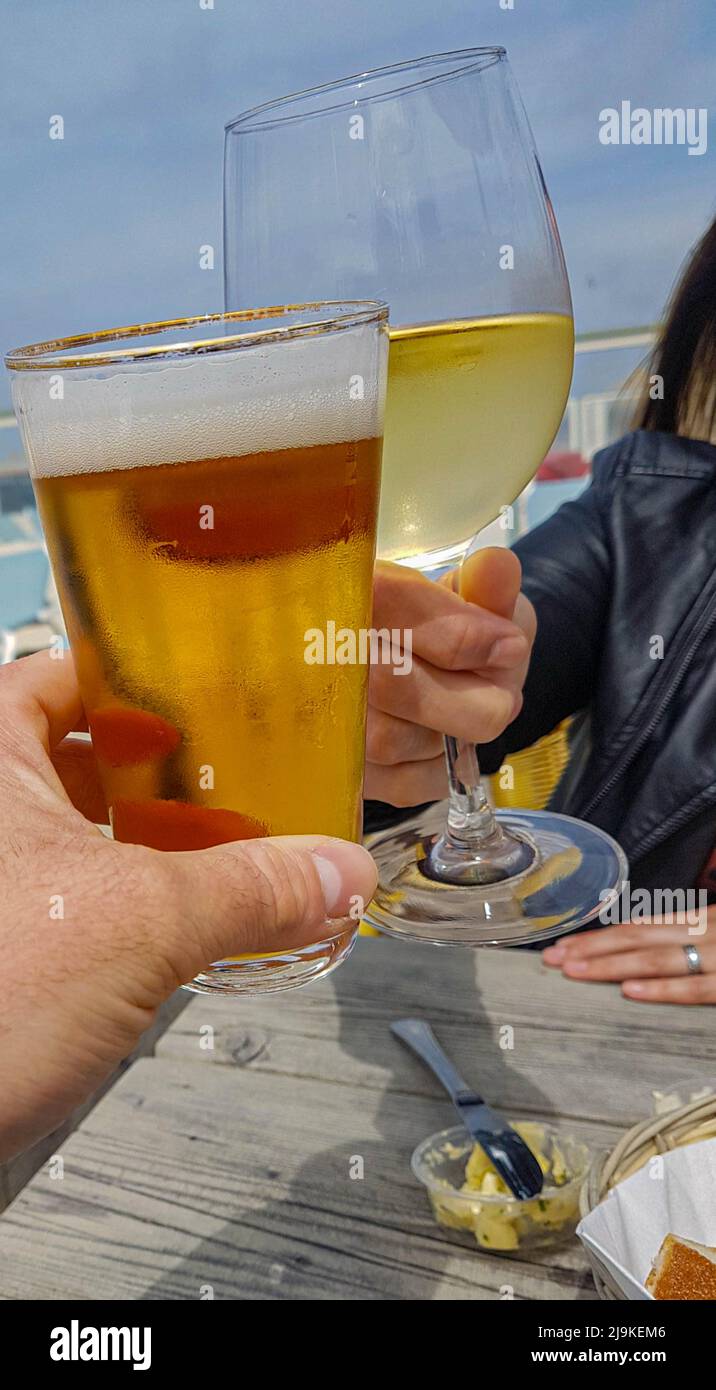 Mano dell'uomo con un bicchiere di birra e una mano della donna con un bicchiere di vino tostando all'esterno sulla terrazza Foto Stock