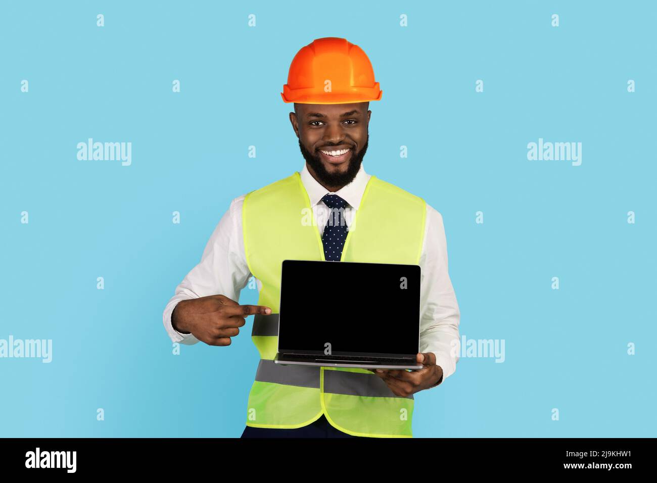 Sorridente lavoratore di costruzioni nere che punta al notebook con schermo vuoto in mano Foto Stock