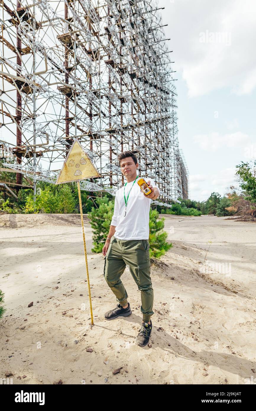 Giovane uomo che tiene un contatore geiger di fronte a un falso pericoloso Radiation Sign Post al Duga Radar in Pripyat Chernobyl Exclusion zone in Ucraina Foto Stock