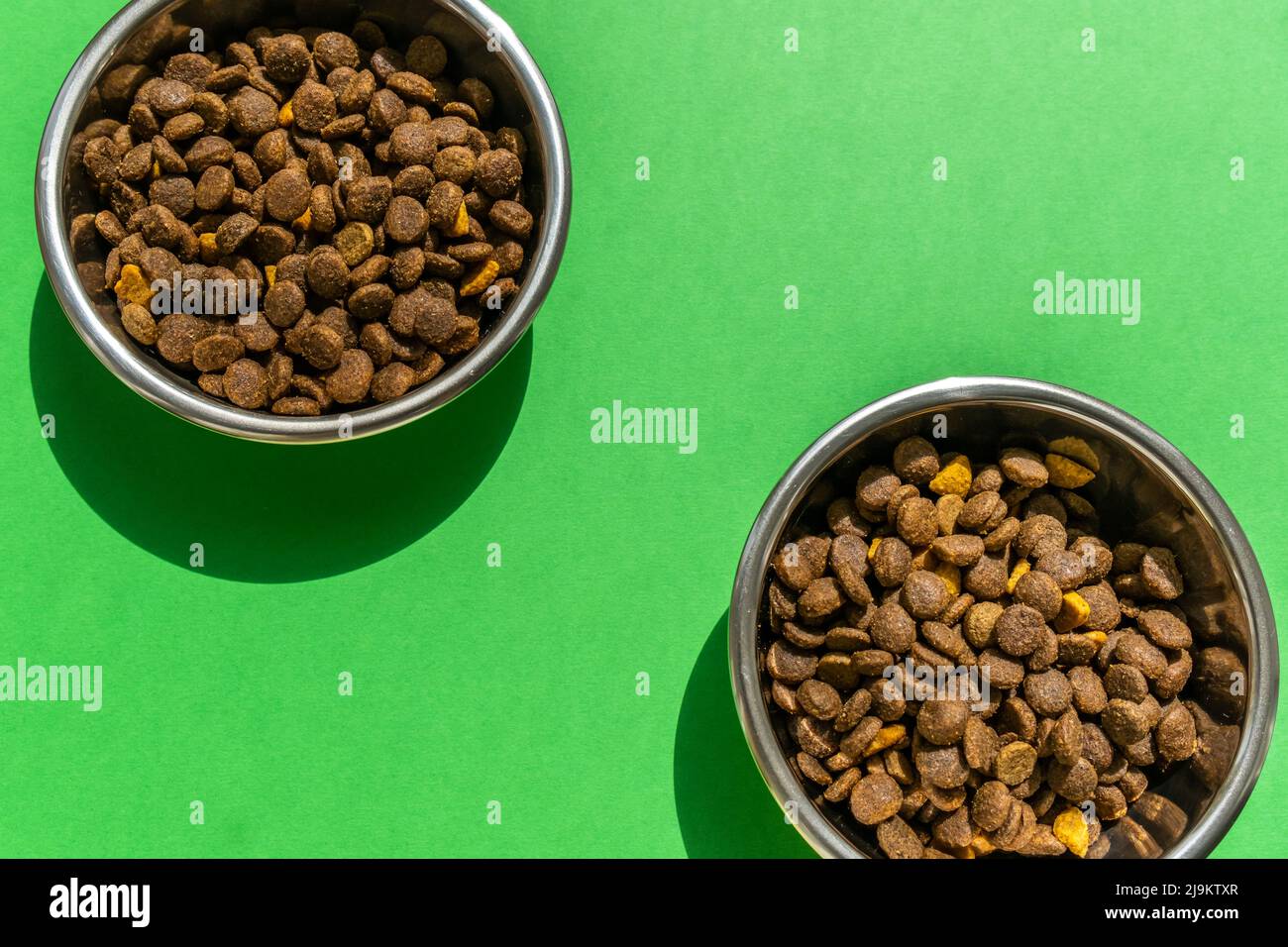 Due ciotole per animali domestici con kibble sullo sfondo verde, immagine ravvicinata Foto Stock