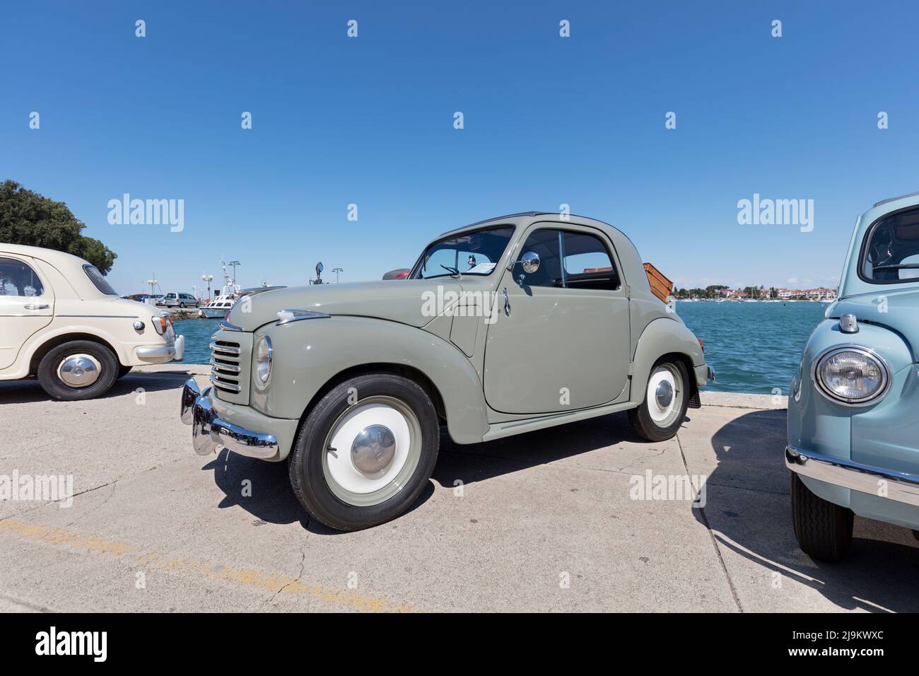 Fiat 600 Topolino e altre auto d'epoca si riuniscono per incontrarsi a Riva Umago, sul lungomare vicino al porto. Umago, Croazia Foto Stock