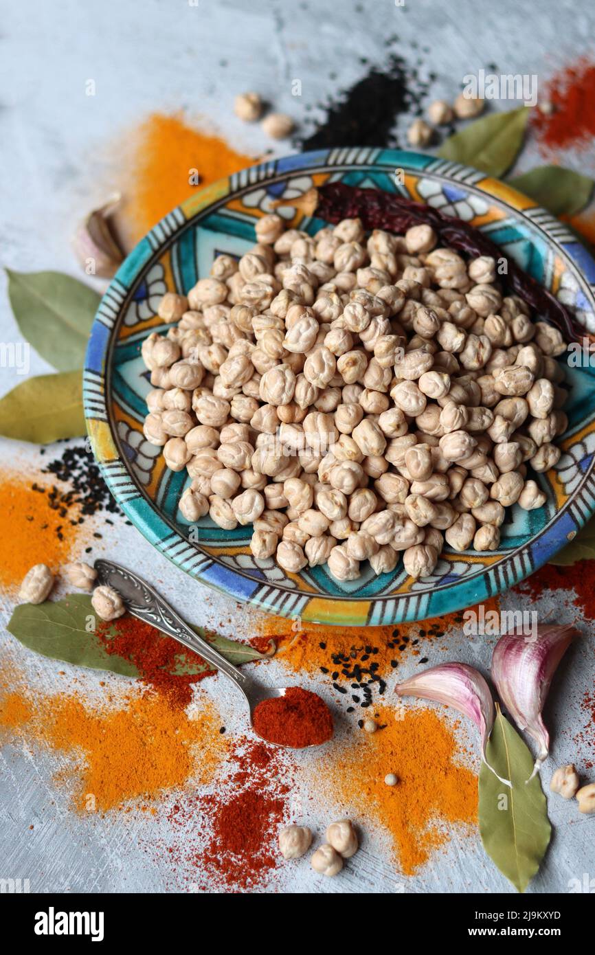 Ceci crudi su piastra di ceramica blu, paprika in polvere, curcuma, pepe e foglia di alloro vista dall'alto foto. Vita morta colorata con spezie diverse. Foto Stock