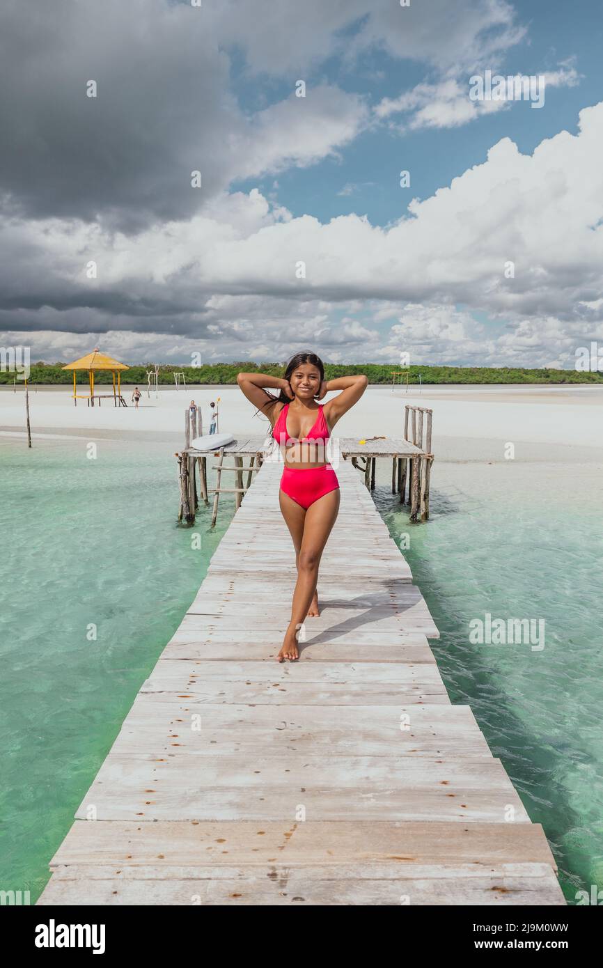 giovane ragazza asiatica che cammina lungo il molo in un costume da bagno bikini rosso con una spiaggia di sabbia bianca sullo sfondo e blu mare turchese Foto Stock